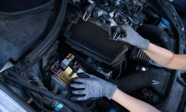 Car repair shop woman checks battery under hood of car