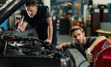 Two mechanics repairing air conditioning system in auto repair shop.